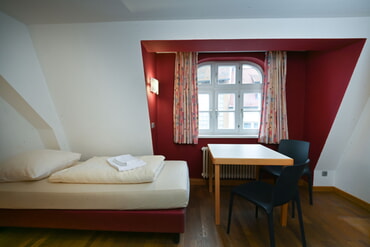 Einzelzimmer mit Bett und Tisch